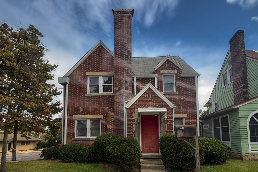 Front of 401 S Highland Ave in Bloomington, IN, a two-story red brick house with a tall front chimney, steep gables and a red front door